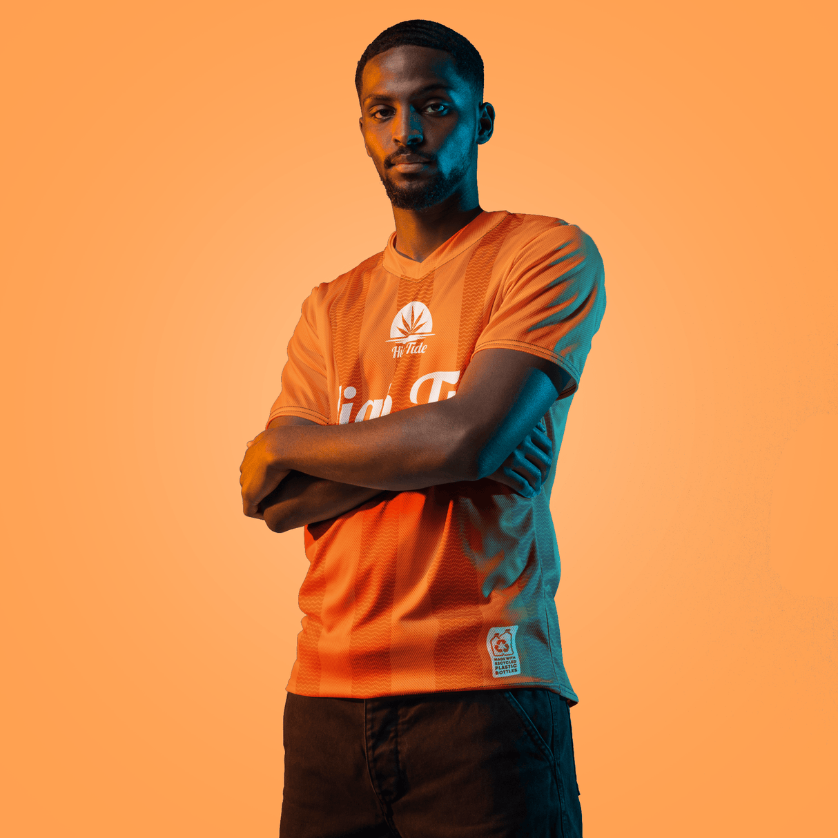 Model wearing a High Tide Soccer Jersey (2024) with an orange backdrop.
