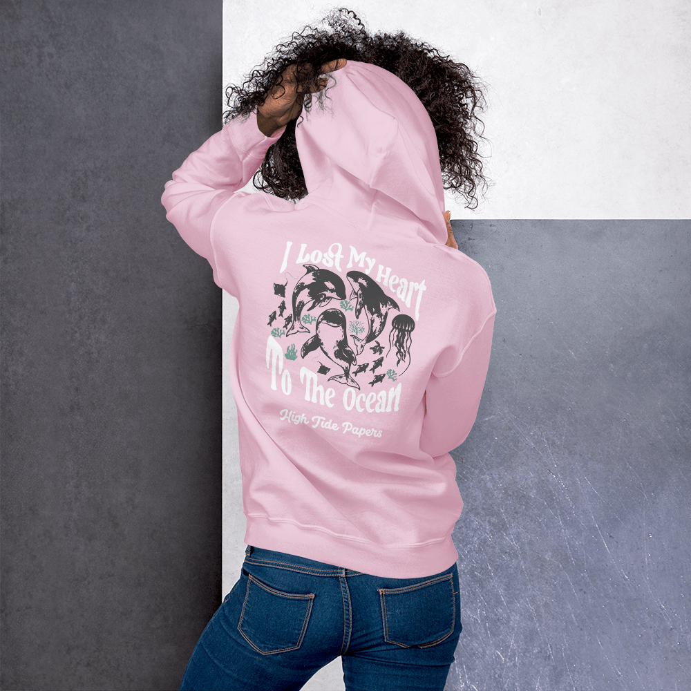 Model wearing High Tide Heart Belongs to the Ocean graphic hoodie, showing the back design graphic white a grey wall backdrop.