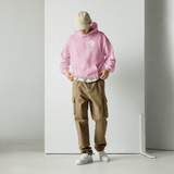 Model wearing High Tide Heart Belongs to the Ocean graphic hoodie, showing the front logo with a white wall backdrop